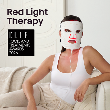 A woman wearing a white LED red light therapy face mask with red illuminated accents sits on a couch in a bright room. Large text reads 'Red Light Therapy,' and an award badge says 'ELLE Tools and Treatments Awards 2026.